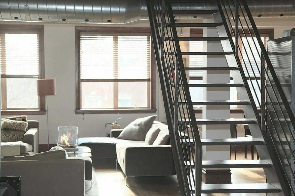 Wohnraum mit offener Treppe, gemütlichem Sofa und großen Fenstern